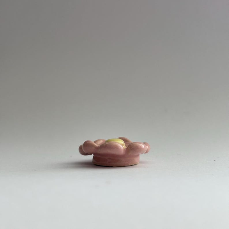 May include: A small pink ceramic flower with a yellow centre. The flower is a decorative object.