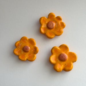 May include: Three ceramic flower-shaped ornaments in a bright orange colour with a smaller peach-coloured centre.