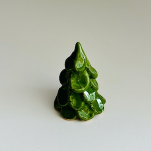 Op de afbeelding: Een klein, groen kerstboom ornament van keramiek. De boom is gemaakt van individuele, afgeronde vormen die lijken op dennennaalden.