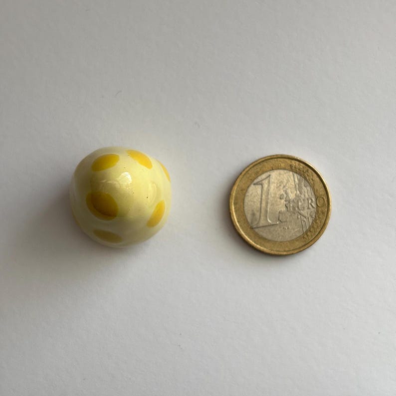 K&ouml;nnte beinhalten: Ein kleines, wei&szlig;es Keramik-Ei mit gelben Punkten. Das Ei ist etwa so gro&szlig; wie eine 1-Euro-M&uuml;nze.