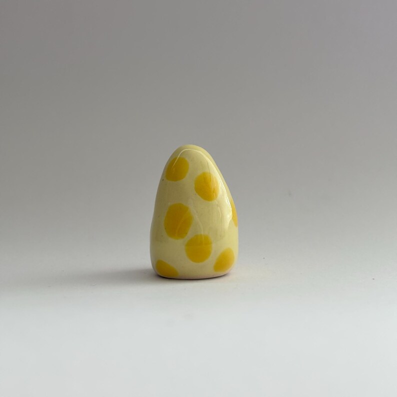 K&ouml;nnte beinhalten: Eine kleine, eif&ouml;rmige Skulptur aus Keramik mit einem gelben und wei&szlig;en Tupfenmuster.