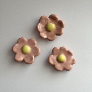 May include: Three pink ceramic flower-shaped buttons with yellow centres.