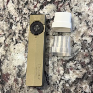 Puede incluir: Una linterna Olight dorada con un botón circular negro y un dial circular negro. Dos accesorios de plástico blanco y translúcido están junto a la linterna. La linterna es rectangular y tiene el logotipo de Olight.