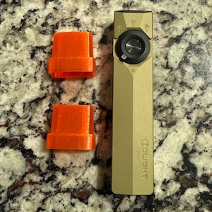 May include: An olive-green Olight Marauder Mini flashlight with a black control dial and two orange 3D-printed covers. The flashlight is rectangular and has the Olight logo printed on it.