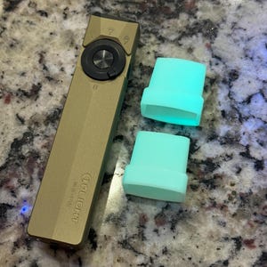 May include: A gold-colored Olight flashlight with a black control dial and two light blue silicone covers. The flashlight has the brand name and logo printed on the side.