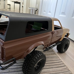 May include: A brown and tan pickup truck with a black hardtop and black wheels. The truck is on a rug with a striped pattern.
