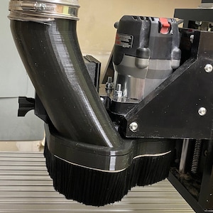 May include: A black dust collection system for a router, with a flexible hose and a brush to capture dust. The system is mounted on a black metal base.