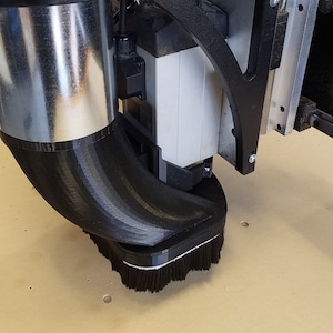 May include: A black 3D printed dust collection shroud with a brush attached to the bottom. The shroud is connected to a silver metal pipe.
