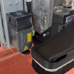May include: Close-up of a black laser cutter with a brush attached to the bottom. The laser cutter is labeled "Opt Lasers PLH-15W".