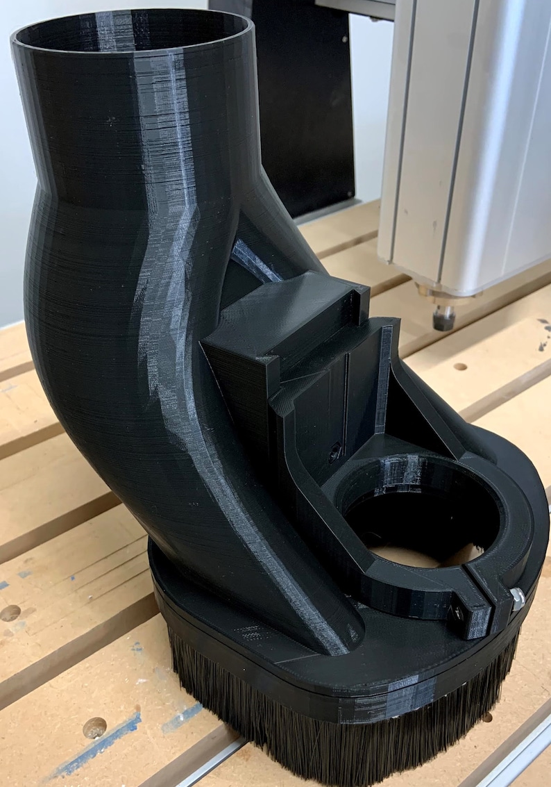 May include: A black 3D printed dust collection system with a brush attachment. The system is designed to be used with a CNC machine.