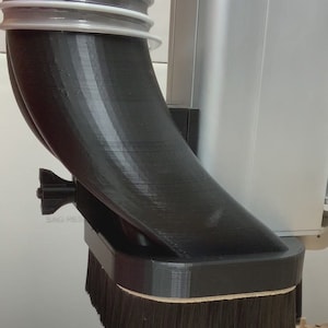 May include: A black 3D printed dust collection system with a brush attachment. The system is connected to a vacuum hose and is designed to collect dust and debris from a woodworking machine.