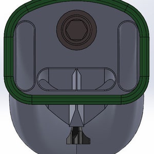 May include: A green and gray plastic object with a hexagonal hole in the center and two rectangular openings on either side. The object has a rounded top and a pointed bottom.