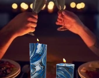 May include: Three blue and white marbled candles with flames burning. The candles are on a dark wooden table with two glasses of champagne in the background.