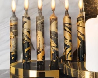 May include: A gold menorah with seven black and gold candles lit. The menorah is on a black and white marble surface.