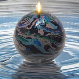 May include: A black, green, and pink marbled candle with a single wick. The candle is floating in a blue liquid.