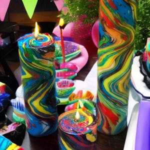 May include: Three colorful, hand-painted candles with a marbled design. The candles are lit and have a yellow, blue, red, and black color scheme.