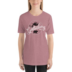 May include: A heather pink t-shirt with a white graphic of a black bear and mountains with the text "Gatlinburg TN" in a white circle.
