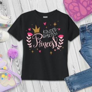 May include: Black t-shirt with a pink and gold design that says "Kindergarten Princess" with a crown, hearts, and stars.