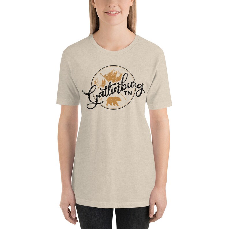 May include: A beige t-shirt with a black and brown graphic design that says "Gatlinburg TN" with a bear and mountains in the design.
