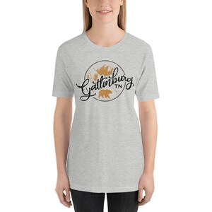 May include: A heather grey t-shirt with a black and brown graphic design featuring the text "Gatlinburg TN" and a bear silhouette.