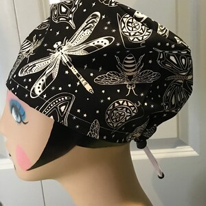 May include: Black scrub hat with a white print of various insects, including a dragonfly, bee, and butterfly. The hat has a white drawstring.
