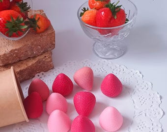 Puede incluir: Imagen de naturaleza muerta con fresas frescas en cuencos de vidrio y objetos decorativos con forma de fresa. Las fresas son de color rojo vibrante con tallos verdes. Los objetos con forma de fresa son de varios tonos de rosa y rojo. El texto "Aroma_meliss" es visible.