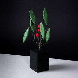 Op de afbeelding: Een zwarte keramische vaas met een groene en rode bloemenarrangement. De vaas heeft een vierkante vorm en een glad oppervlak. De bloemen zijn gemaakt van vilt en zijn in een moderne stijl gerangschikt.