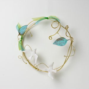 May include: A gold wire wreath with two white porcelain doves and two turquoise blue leaves. The wreath is decorated with green and blue ribbon.