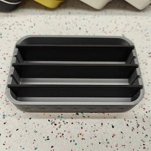 May include: A gray rectangular organizer with three black dividers. The organizer has a star pattern along the bottom edge. The product is designed to hold small items.