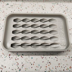 May include: A light gray rectangular organizer with multiple hexagonal slots. The text "HEX BITS" is printed on the side. The organizer is designed to hold small items, likely tools or hardware.