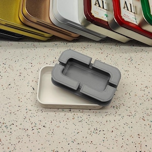 May include: A rectangular white tray with a textured base and a removable gray top piece featuring a central rectangular cutout and four corner notches. The gray top piece has a visible layered texture consistent with 3D printed construction.