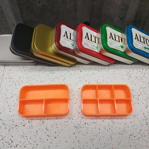 May include: A set of eight empty Altoids tins in various colors, including silver, black, gold, red, green, and blue. The tins are stacked on top of each other. The tins are all the same size and shape. The tins are all labeled with the word "Altoids".