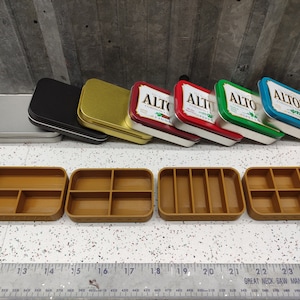 May include: Six small, rectangular metal tins with various colors and designs. The tins are labeled with the word "Altoids" and different flavors.  The tins are arranged in a row on a wooden surface.  Below the tins are six small, rectangular wooden boxes with compartments.