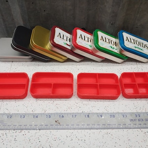 May include: Four red plastic trays with different numbers of compartments. The trays are arranged in a row from left to right, with the tray on the left having two compartments, the next tray having three compartments, the next tray having four compartments, and the tray on the right having six compartments.  A ruler is in the bottom of the image.