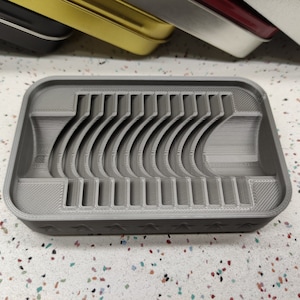 May include: A gray plastic tray with a series of curved ridges, designed for holding and organizing small items.