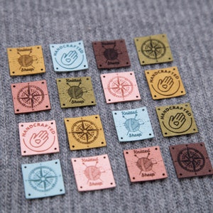 K&ouml;nnte beinhalten: Sortiment von 15 quadratischen Leder-Etiketten mit verschiedenen Designs, darunter ein Kompass, eine Hand mit einem Herzen und ein gestricktes Schaf. Die Etiketten sind in verschiedenen Farben, darunter Braun, Rosa, Blau und Gelb.