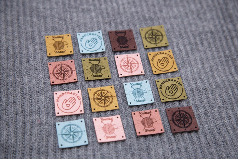 K&ouml;nnte beinhalten: Sortiment von 15 quadratischen Leder-Etiketten mit verschiedenen Designs, darunter ein Kompass, eine Hand mit einem Herzen und ein gestricktes Schaf. Die Etiketten sind in verschiedenen Farben, darunter Braun, Rosa, Blau und Gelb.