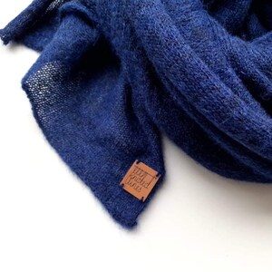 K&ouml;nnte beinhalten: Ein weicher, blauer Strick Schal mit einem braunen Leder Etikett, auf dem "Woven Fins" steht.
