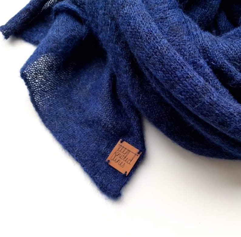 K&ouml;nnte beinhalten: Ein weicher, blauer Strick Schal mit einem braunen Leder Etikett, auf dem "Woven Fins" steht.