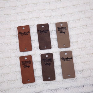 Pode incluir: Seis etiquetas de couro marrom com furos para um cord&atilde;o. As etiquetas t&ecirc;m textos diferentes, incluindo "Handmade by Olivia" e "Handmade with love by Mary".