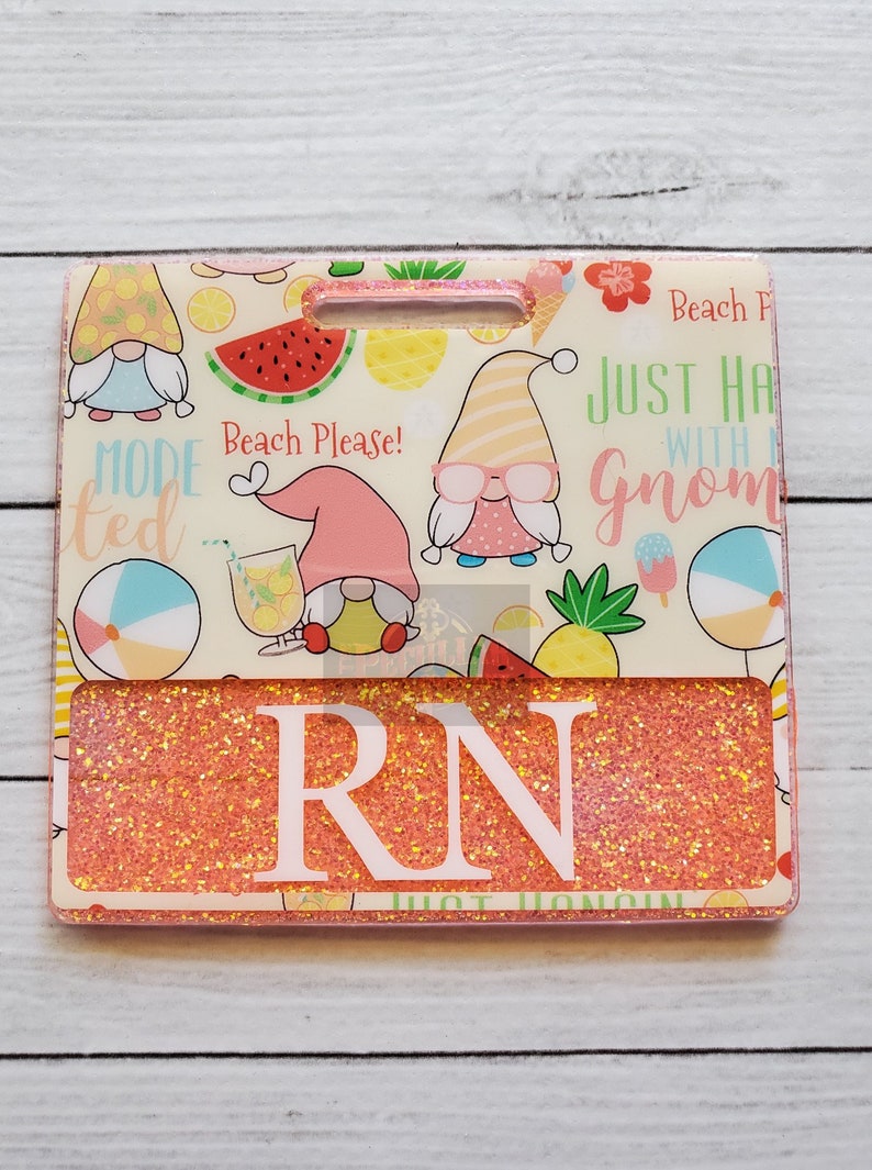 May include: A pink and white glitter badge holder with a summer gnome theme. The badge holder has a clear window for displaying a name tag. The text on the badge holder reads "Beach Please!" and "Just hang with a gnome".