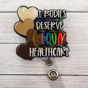 Puede incluir: Un portagafete negro y plateado con purpurina con tres corazones en diferentes tonos de piel. El texto en el portagafete dice "Todos los cuerpos merecen atención médica igualitaria".