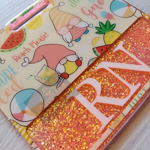 May include: A pink and white glitter keychain with the text "Beach Please!" and "Just hang with gnomes". The keychain also features a pink and yellow gnome, a watermelon, a pineapple, and a beach ball.