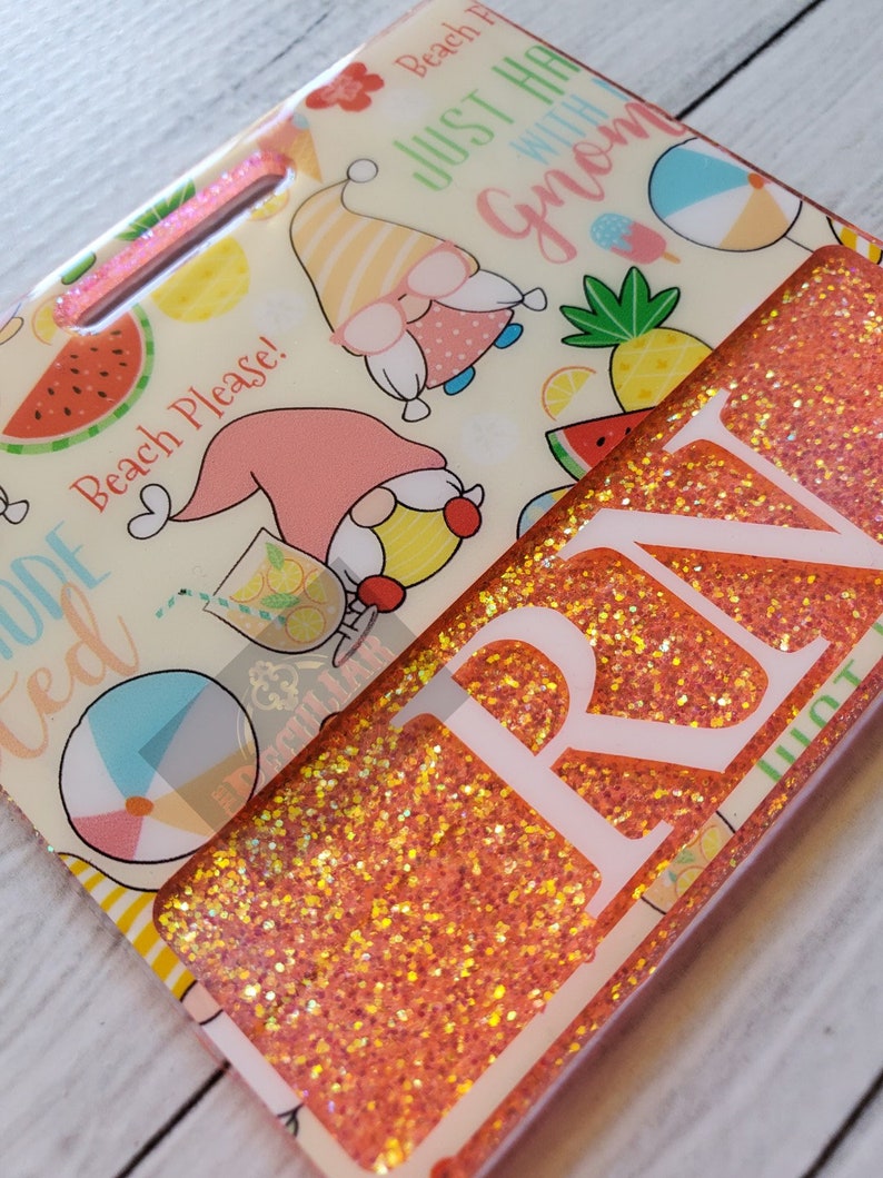 May include: A pink and white glitter keychain with the text "Beach Please!" and "Just hang with gnomes". The keychain also features a pink and yellow gnome, a watermelon, a pineapple, and a beach ball.