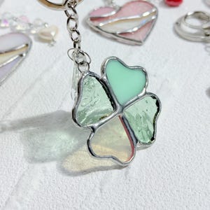 May include: A silver charm keychain with a four-leaf clover design. The clover is made of stained glass with green, light green, and iridescent glass pieces.