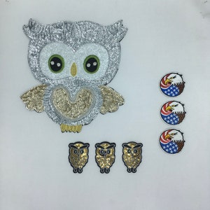 May include: A set of iron-on patches featuring a silver and gold sequined owl, three smaller gold sequined owls, and three embroidered American eagle patches.