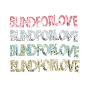 Könnte beinhalten: Vier Reihen des Satzes "Blind for Love" in verschiedenen Farben. Die oberste Reihe ist rosa, die zweite Reihe ist silber, die dritte Reihe ist blau und die unterste Reihe ist gold. Jede Reihe besteht aus Pailletten.