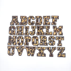 May include: A set of 26 uppercase letters in a leopard print design. The letters are outlined in black and have a gold glitter effect. The letters are arranged in alphabetical order.