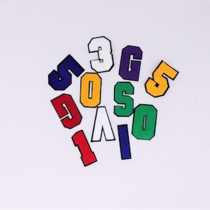 May include: A collection of felt iron-on patches in various colors, featuring the numbers 1, 3, 5, 6, 7, 8, 9, and 0. The patches are in a variety of colors, including red, white, blue, green, yellow, and purple.