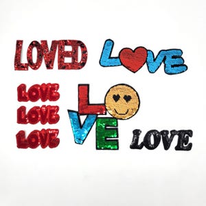 May include: Assortment of colorful iron-on patches featuring the word "LOVE" in various styles and colors, including a smiley face, a heart, and a stacked design.